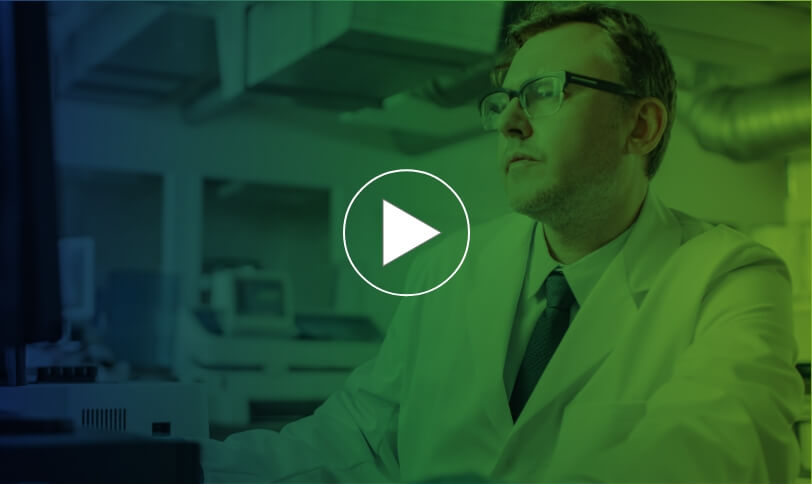 clickable video thumbnail - a man in a lab coat sitting at a work station reviewing a monitor